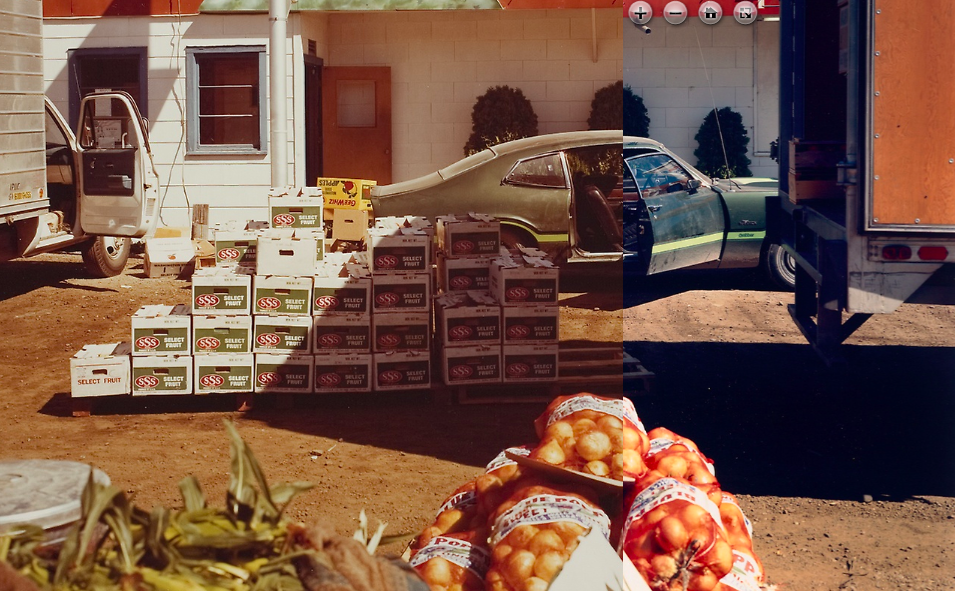 A stack of boxes of oranges next to a truck with oranges in the foreground and a car and building in the background. Image has the warm tones of 1970s film.